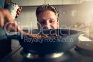 Something smells good. Shot of young man watching his mother cooking on the stove in their kitchen at home.