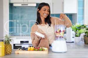 My morning source of energy is a fresh smoothie. Shot of a young woman preparing a healthy smoothie at home.