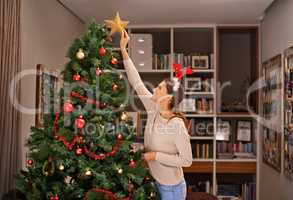 Spreading love and light with her Christmas star. Shot of a beautiful young woman decorating her Christmas tree at home.