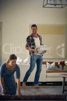 Do you need any help with that. Shot of a young beautiful woman rolling up a carpet while her handsome husband is carrying books at home.