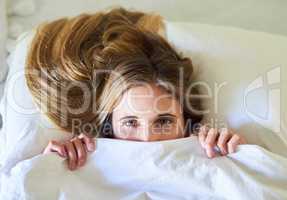 Theres no way Im leaving this bed today. Portrait of a playful young woman hiding under the covers in her bed.
