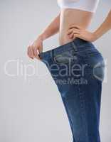 You can achieve this too. Cropped shot of a woman showing off her weightloss with a large pair of trousers.
