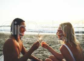We can still be kids. Shot of a young happy couple having fun and lighting sparklers while on a date on the beach at sunset.