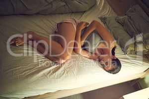 Late night pains. Shot of a young woman clutching her stomach while lying on her bed in her bedroom.
