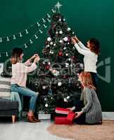 We are all doing our part. Shot of three attractive middle aged women decorating a Christmas tree together at home.