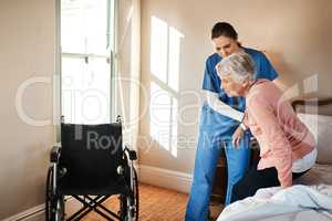 Simple movements aren't so simple anymore. Shot of a young nurse helping a senior woman get up from her bed in a nursing home.