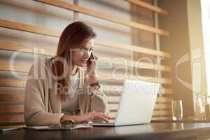 Setting up business opportunities at the cafe. Shot of a young woman talking on a cellphone while working on her laptop in a cafe.