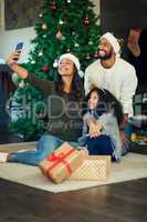 Happy family memories warm those cold December days. Shot of a happy young family taking selfies while opening Christmas presents at home.