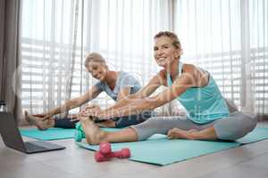 Our golden sea, making memories. Portrait of two mature women watching an exercise tutorial on a laptop while stretching on the floor at home.