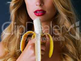 Because who doesnt like a tasty banana now and then. Cropped studio shot of a young woman eating a banana suggestively against a dark background.