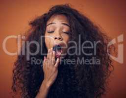 Im tired of haircare products thats not doing what theyre supposed to do. Shot of a young woman with curly hair yawning against an orange background.