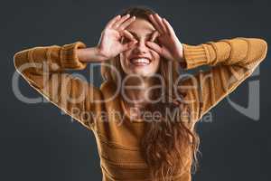 You cant spoil her mood. Studio portrait of a cheerful young woman making a face with her hands while standing against a dark background.