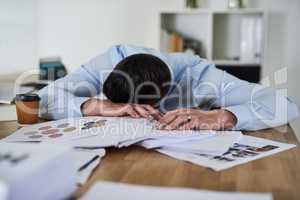 Its another overwhelming day in the office. Shot of a tired young businessman with his head down on a pile of paperwork in an office.