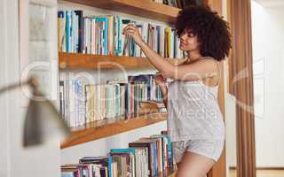 Tattooed trees for a world in a binder. Shot of an attractive young woman browsing a book shelf at home.