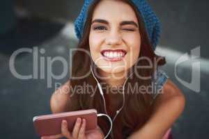 She found the right song for the occasion. Portrait of a carefree young woman seated on the floor while listening to music through her earphones outside during the day.