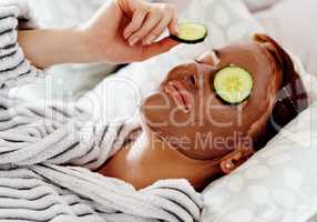 My face deserves this treatment. Cropped shot of an attractive young woman placing a slice of cucumber on her face while pampering herself in her bedroom at home.