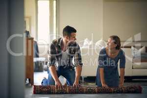 Im here to help you with whatever you need. Shot of a young married couple rolling up a carpet together at home.