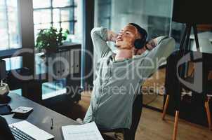 Listening to my favourite podcast. Shot of a young businessman wearing headphones while taking a nap in an office.