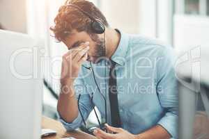 Dealing with difficult clients. Shot of a young man experiencing stress while working in a call center.