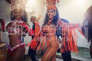 All the right moves. Portrait of two female dancers wearing vibrant costumes while dancing to music inside of a busy nightclub.