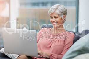 That looks quite amazing. Shot of a cheerful mature woman using her laptop while relaxing on her sofa ta home.