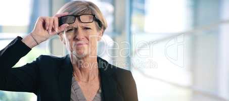 Excuse my poor eyesight. Portrait of a mature businesswoman frowning while holding a pair of spectacles in an office.