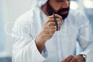 Seeking divine intervention. Cropped shot of a young businessman dressed in Islamic traditional clothing holding prayer beads while working in his office.