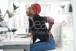 Her back is taking most of the strain. Cropped shot of an attractive young businesswoman holding her back in pain while sitting at her desk in the office.