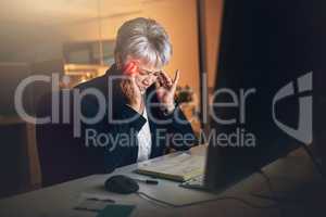 When stress invades the work space. Shot of a mature businesswoman experiencing a headache during a late night at work.