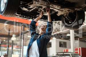 Theres nothing quite like being able to fix something with your bare hands. Shot of a female mechanic working under a lifted car.