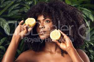 Who said plant based cant be as potent as conventional skincare. Shot of a beautiful young woman holding juicy lemon halves against a leafy background.