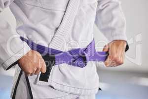 Ready to fight. Cropped shot of an unrecognizable man tying a purple belt around hist waist while in full jiu jitsu gi.