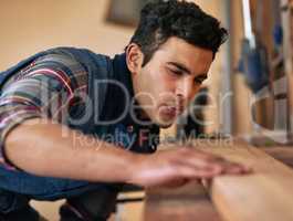He loves doing it himself. Shot of a focused handyman examining a piece of wood while working in his workshop.