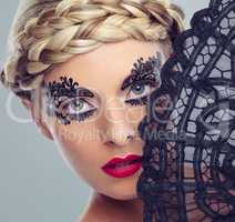 Her beauty belays her shyness. Closeup studio shot of a beautiful woman with intricate makeup holding a fan in front of her face.