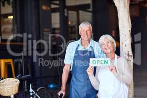 Come on down and see what we have to offer. Portrait of a happy senior couple holding up an open sign in their store.