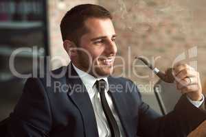 Suave and successful. Shot of a stylish businessman smoking a pipe in the office.