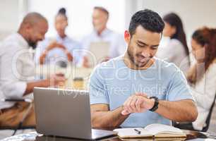 He knows how to manage his time productively and efficiently. Shot of a young businessman checking the time while working on a laptop in an office with his colleagues in the background.