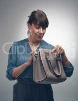 What business move will she pull out of her bag today. Studio shot of a senior woman looking for something in her handbag against a grey background.