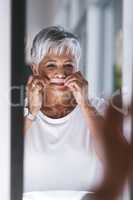 She makes sure she is looking flawless everyday. Portrait of a cheerful mature woman waxing her moustache while looking into a mirror at home.