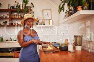 God knows ive time to give. Portrait of a young beautiful woman wearing a sunhat while slicing fruit in the kitchen at home.
