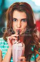 Brain freeze, that was a bit too much at once. Shot of a beautiful young woman drinking a milkshake in a diner.