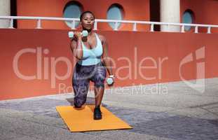 Your only worthy competitor is YOU. Shot of a young woman on a gym mat using dummbells against an urban background.