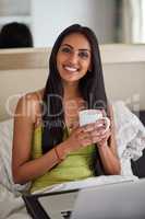 Who needs to leave the bed with high speed internet. Shot of a relaxed young woman using a laptop and drinking coffee in bed.