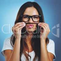 Showing her quirky side. Studio portrait of an attractive young woman playfully making a moustache with her hair against a blue background.