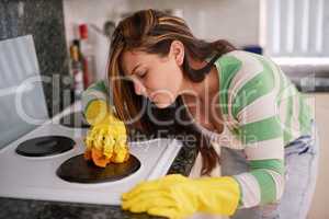 This grime just wont come off. Shot of a young woman cleaning a kitchen stove top.