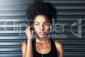 Plug in and get moving. Shot of a sporty young woman listening to music while exercising against a grey background.