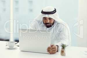 Focused on the task at hand. Cropped shot of a young businessman dressed in Islamic traditional clothing working on his laptop while sitting in the office.