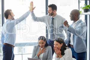 Our greatest accomplishments have come from team work. Shot of a group of businesspeople celebrating while using a laptop in an office at work.