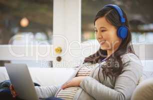 Unwinding online. Shot of a pregnant woman wearing headphones while using a laptop at home.