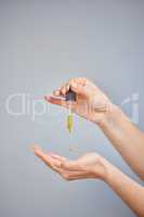 Just one drop does the trick. Shot of a young woman taking serum from a dropper against a grey background.